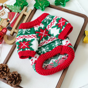 Knitted dog sweater with Christmas pattern on a white surface with decorative items.