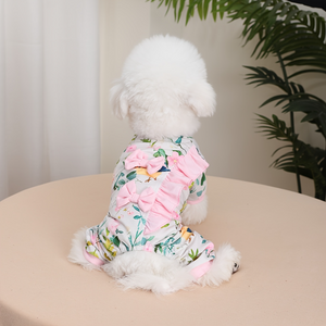 Small dog wearing a floral outfit with ruffles on a beige surface.