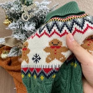Knitted dog sweater with gingerbread design held by a hand, Christmas tree in the background