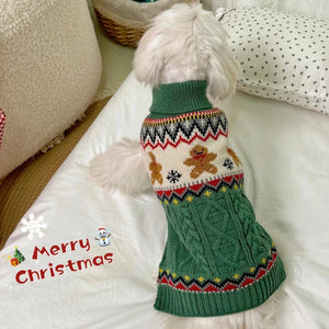 Dog wearing a green Christmas sweater with gingerbread men design on a white couch.