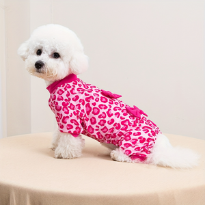Small white dog wearing a pink leopard print outfit on a beige surface.