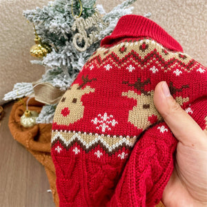 Red knitted sweater with reindeer pattern held by a hand, Christmas tree in the background