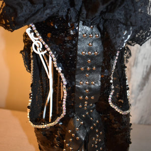 This handmade “Elektra” dress features glittering black sequins, silver beaded leather trim down the midline and cascading black lace at the neck.