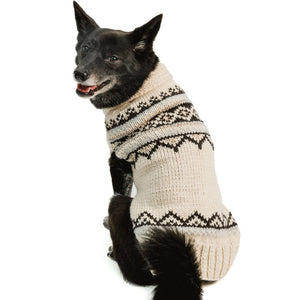 A black dog wearing a cream and black knit sweater with a Fair Isle pattern, photographed against a solid white background.