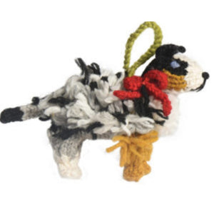 A handmade crocheted Australian Shepherd ornament with a black and white shaggy body, a red bow on a plain white background.