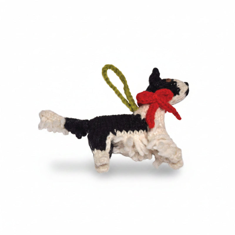 A handmade crochet Border Collie dog ornament in black and white yarn with a red bow and an olive green hanging loop, shown against a plain white background.