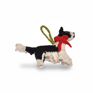 A handmade crochet Border Collie dog ornament in black and white yarn with a red bow and an olive green hanging loop, shown against a plain white background.
