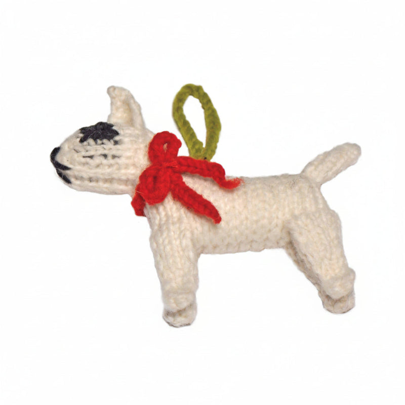 A hand-knitted white Bull Terrier hristmas ornament with a red bow, black nose/eyes, and a green hanging loop, shown against a plain white background.