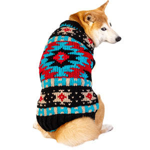A Shiba Inu dog wearing a colorful knit sweater with a red, blue, black, and beige geometric pattern, shown from the back against a white background.