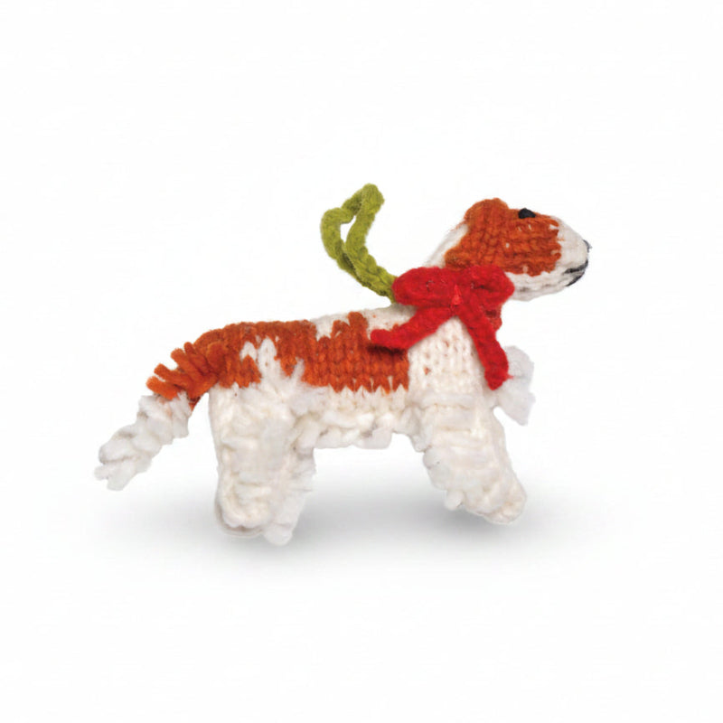 Knitted Cavaier dog ornament with red bow and green tail on a white background