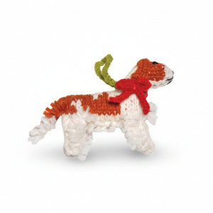 A handmade knitted Cavlier dog ornament or plush toy in white and rust-orange yarn, wearing a red bow and green antlers, isolated on a white background.