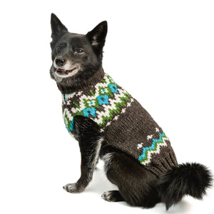 A black dog wearing a knitted pet sweater with a brown base and a colorful Fair Isle pattern of blue, green, and white, photographed against a solid white background.
