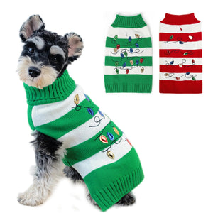 Dog wearing a green and white striped sweater with Christmas lights, next to two other sweaters.