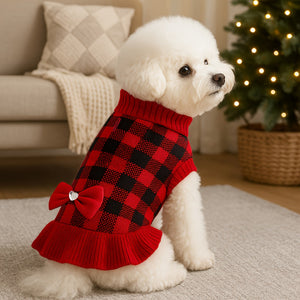 White Bichon dog wearing a red and black checkered sweater with a bow in a living room.