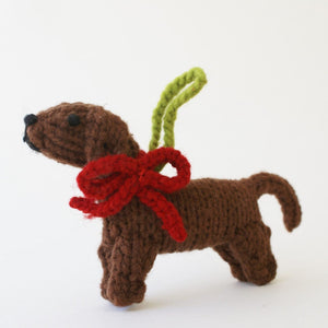 Knitted dog ornament with a red bow and green branch on a white background