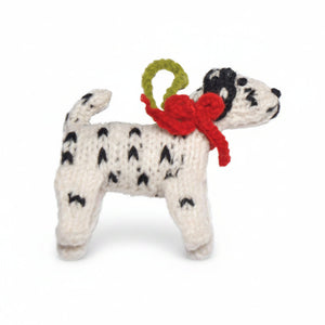 A hand-knit dalmatian dog ornament wearing a red bow and green loop on a white background.
