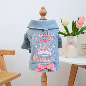 Denim jacket with 'Daddy's Princess' embroidery on a wooden stand with a vase of flowers in the background.