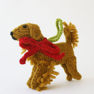 Knitted Golden Retriever ornament with a red bow on a white background