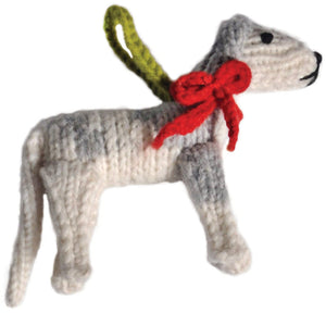 A hand-knit dog-shaped ornament or plush toy in white and gray, with a bright red bow around its neck and a green hanging loop, shown on a plain white background.