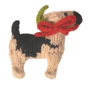 A knitted dog ornament with a tan and black pattern, wearing a red bow and green antler-like decoration, shown on a plain white background.