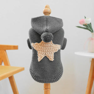 Gray knitted dog sweater with a beige star design on a wooden stand against a light background.