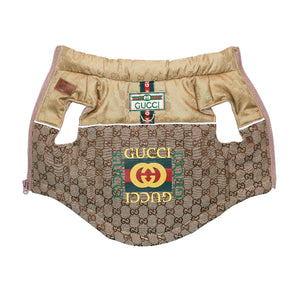 A luxury Gucci dog puffer coat made of beige canvas with a gold satin neck panel and pink piping, featuring a central embroidered logo patch.