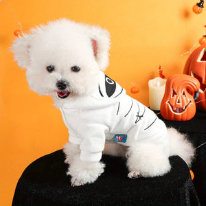 Small white dog wearing a Halloween costume with pumpkins and candles in the background.