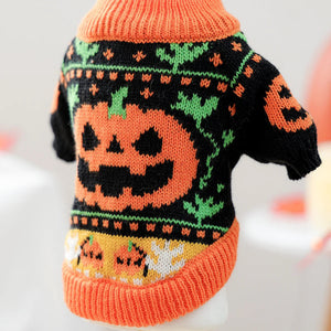 A small knit pet sweater with a Halloween theme, featuring a large orange jack-o'-lantern on a black background with green leaf patterns and orange ribbed trim.