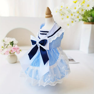 Pet dress with blue and white stripes and a bow on a mannequin against a blurred floral background.