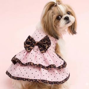 Dog wearing a pink polka dot dress with a leopard print bow on a pink background