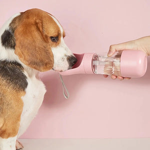 Dog drinking from a pink pet water bottle held by a person on a pink background