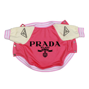 A pink and cream dog jacket styled like a Prada sport coat, featuring 'PRADA MILANO' printed in black on the front, with pink and cream striped ribbed cuffs and hem.