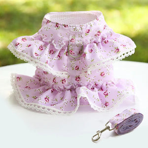 Floral-patterned purple pet harness and leash set on a white surface with a blurred green background