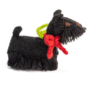 Knitted black dog toy with a red bow and green collar on a white background