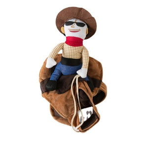 A plush cowboy doll wearing a brown hat, black sunglasses, a red scarf, a tan plaid shirt, and blue pants, posed sitting on a brown saddle against a plain white background.