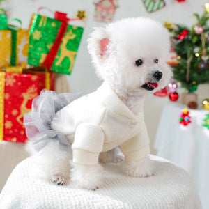 Small white dog in white snowman dress with gray tutu in a festive setting with Christmas decorations