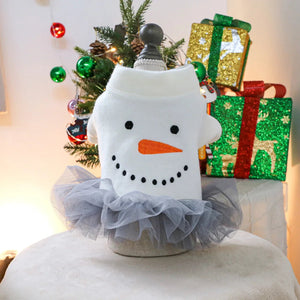 Decorative snowman dog dress with a tutu in front of a Christmas tree and presents.