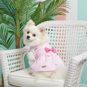 Pink and white striped dress with a large pink bow and small green alligator patterns on a white background