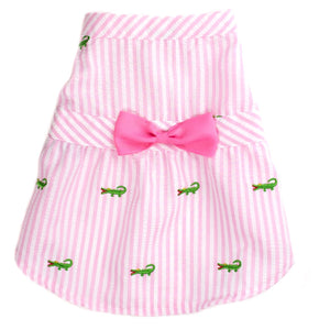 Pink and white striped dog dress with a large pink bow and small green alligator patterns on a white background