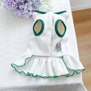 White tennis dog dress with green trim on a white surface with purple flowers in the background