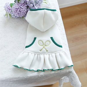 White pet dress with green trim and embroidered design on a white surface with flowers.