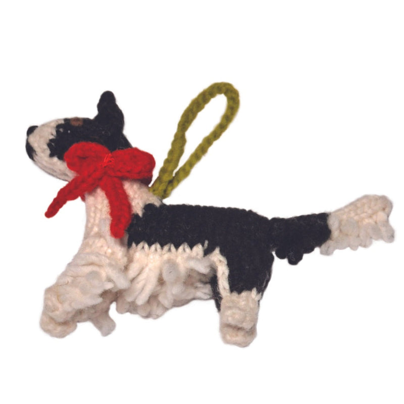 A handmade crochet Border Collie dog ornament in black and white yarn with a red bow and an olive green hanging loop, shown against a plain white background.