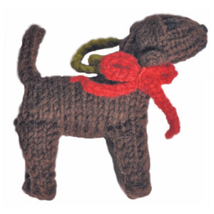 A small hand-knit dog ornament or plush toy in dark brown yarn, wearing a bright red bow and collar with an olive green leash, isolated on a white background.