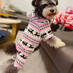 Dog wearing a pink and black deer patterned deer pjs sitting on a coUCH